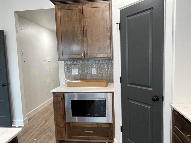 kitchen featuring baseboards, decorative backsplash, light wood finished floors, and stainless steel microwave