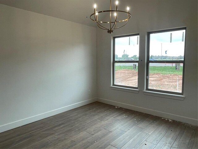 empty room with baseboards, dark wood-style floors, and a notable chandelier