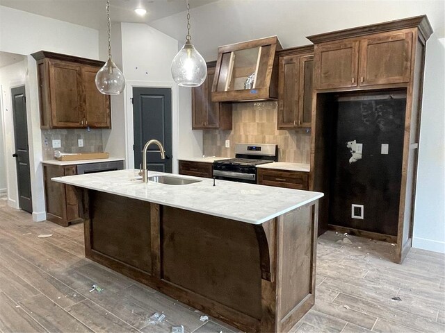 kitchen with stainless steel range with gas cooktop, light countertops, light wood-type flooring, tasteful backsplash, and a sink
