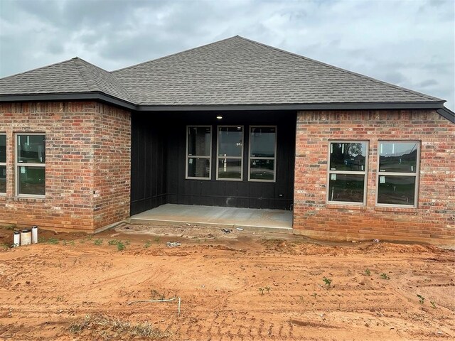 rear view of house with brick siding and roof with shingles
