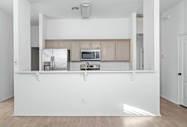 3833 Ives Way, Norman, OK 73072 - kitchen with stainless steel appliances, a breakfast bar, decorative backsplash, and light wood-style flooring