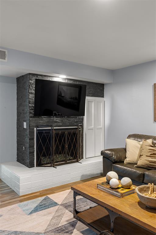 living area with a fireplace with raised hearth, visible vents, and wood finished floors