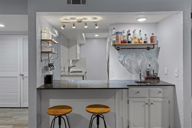 bar with light wood finished floors, wet bar, a sink, and visible vents