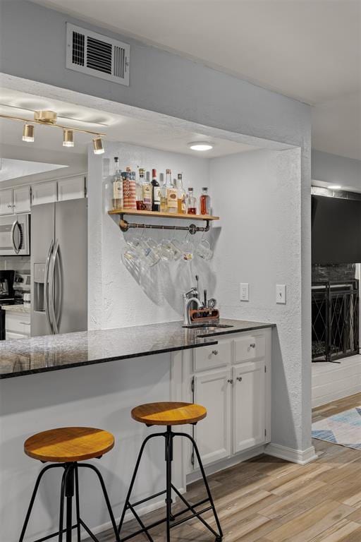 bar with indoor bar, visible vents, a sink, light wood finished floors, and stainless steel appliances