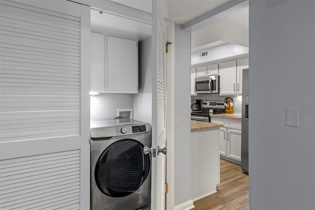 washroom featuring light wood-style floors, washer / clothes dryer, visible vents, and cabinet space