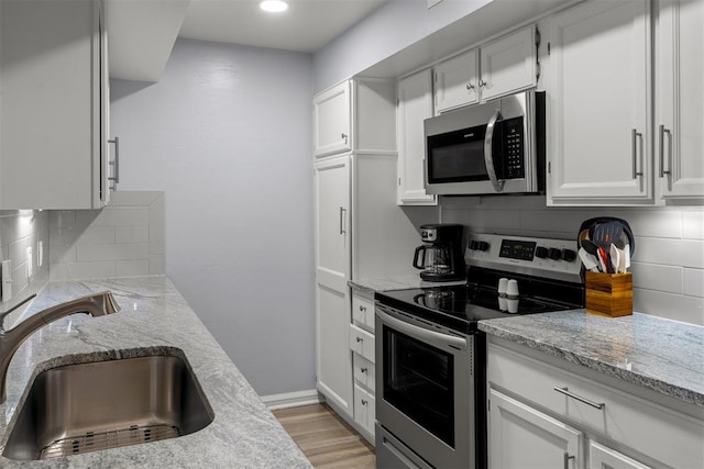 kitchen featuring a sink, white cabinetry, stainless steel appliances, decorative backsplash, and light stone counters