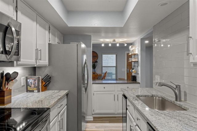 kitchen featuring light wood-style flooring, white cabinets, a sink, stainless steel appliances, and backsplash