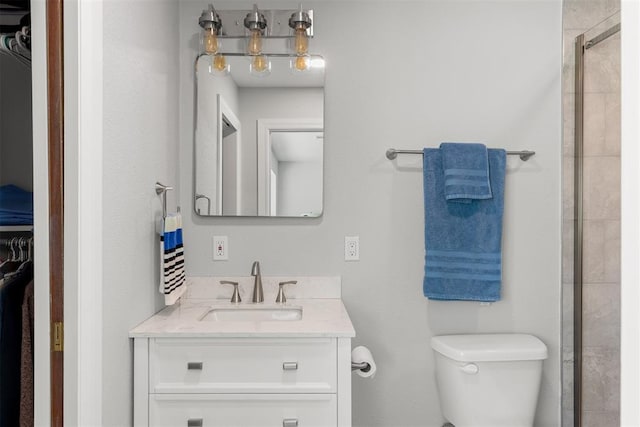 bathroom with a spacious closet, tiled shower, vanity, and toilet