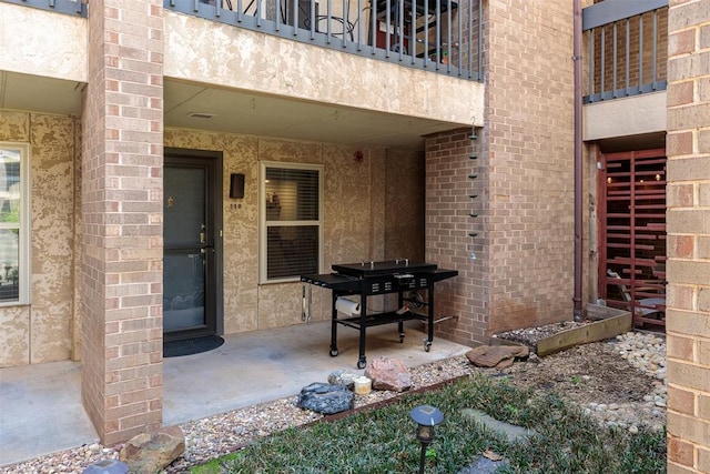 view of exterior entry with a patio area, brick siding, and a balcony