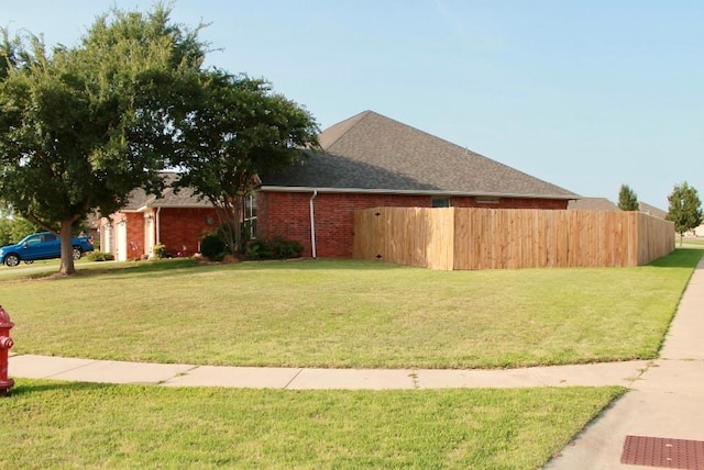 view of side of property with brick siding, fence, roof with shingles, a lawn, and an attached garage