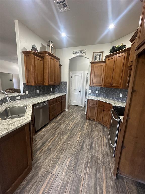 kitchen with visible vents, a sink, light stone counters, dark wood-style floors, and stainless steel appliances