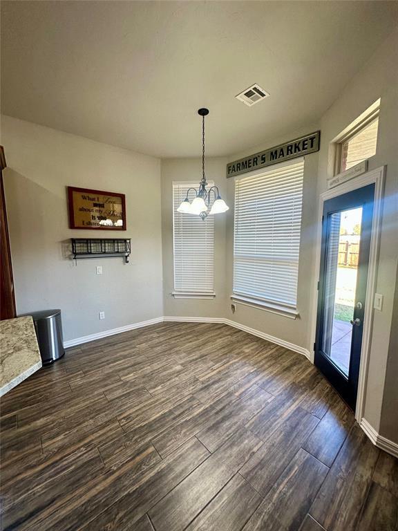 unfurnished dining area featuring an inviting chandelier, visible vents, dark wood-style flooring, and baseboards