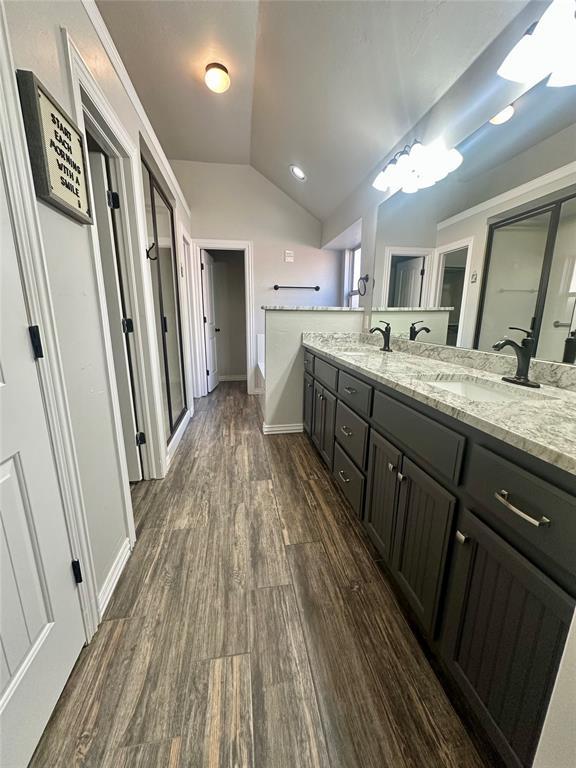 full bath featuring wood finished floors, lofted ceiling, double vanity, a sink, and a shower stall