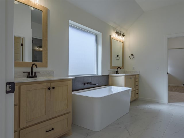 2292 NW 34th St, Newcastle, OK 73065 - bathroom featuring marble finish flooring, vaulted ceiling, a freestanding bath, two vanities, and baseboards