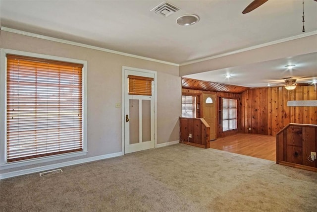 interior space with carpet flooring, a ceiling fan, visible vents, and wood walls