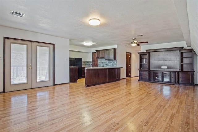 kitchen with dark brown cabinetry, open floor plan, light wood-style flooring, and freestanding refrigerator