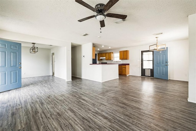 unfurnished living room featuring visible vents, ceiling fan with notable chandelier, a textured ceiling, and dark wood-type flooring