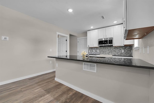 311 N 7th St, Sayre, OK 73662 - kitchen featuring stainless steel microwave, white cabinetry, dark wood-style floors, decorative backsplash, and dark stone countertops