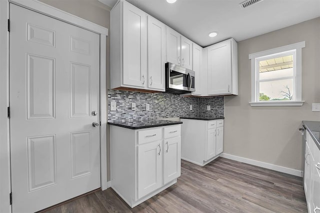 311 N 7th St, Sayre, OK 73662 - kitchen with stainless steel microwave, tasteful backsplash, wood finished floors, dark countertops, and white cabinetry