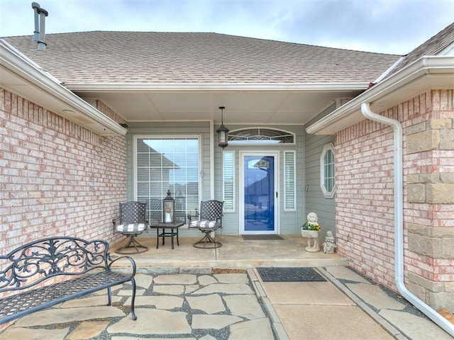 view of exterior entry featuring brick siding and roof with shingles