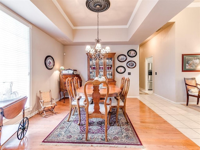 dining area featuring light wood-type flooring, a raised ceiling, an inviting chandelier, crown molding, and baseboards