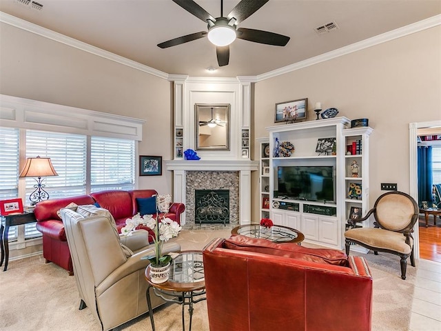 living room featuring visible vents, a fireplace with raised hearth, ornamental molding, and a ceiling fan