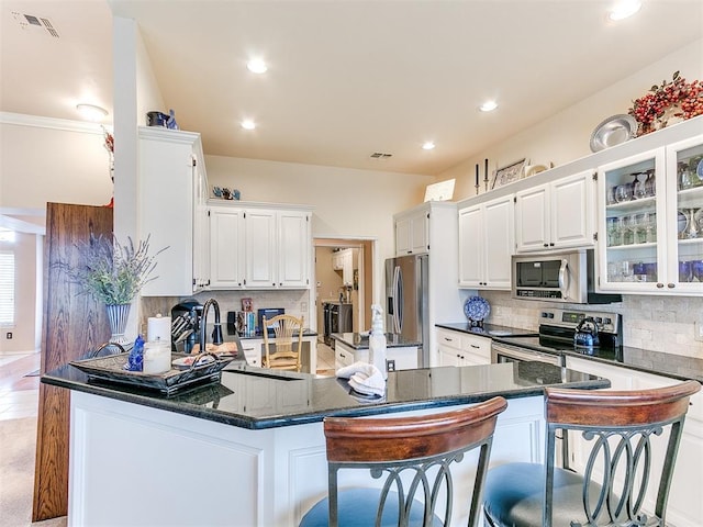 kitchen with a peninsula, a sink, stainless steel appliances, white cabinets, and backsplash