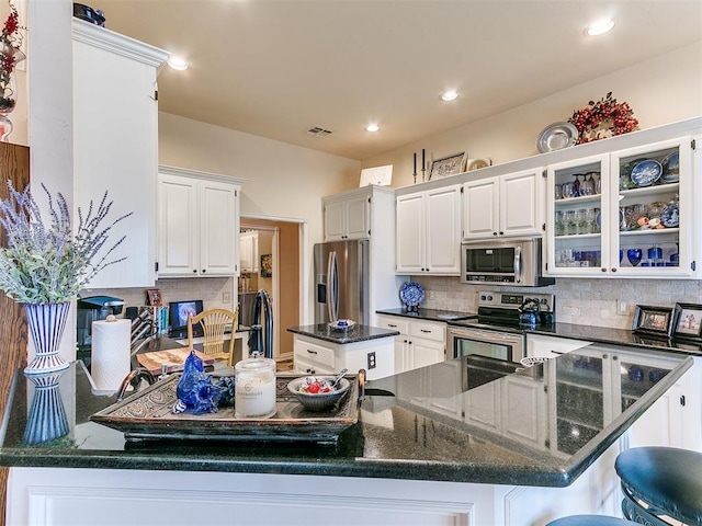kitchen with visible vents, tasteful backsplash, stainless steel appliances, a peninsula, and glass insert cabinets