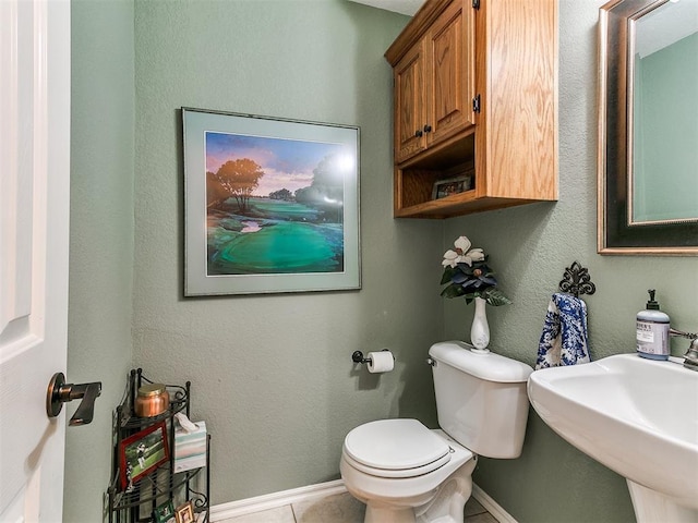 half bath featuring a sink, baseboards, toilet, and tile patterned flooring