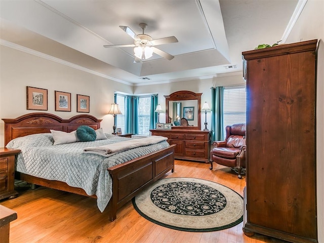 bedroom with a tray ceiling, light wood-style flooring, and crown molding