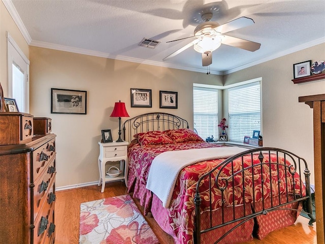 bedroom with crown molding, wood finished floors, visible vents, and baseboards