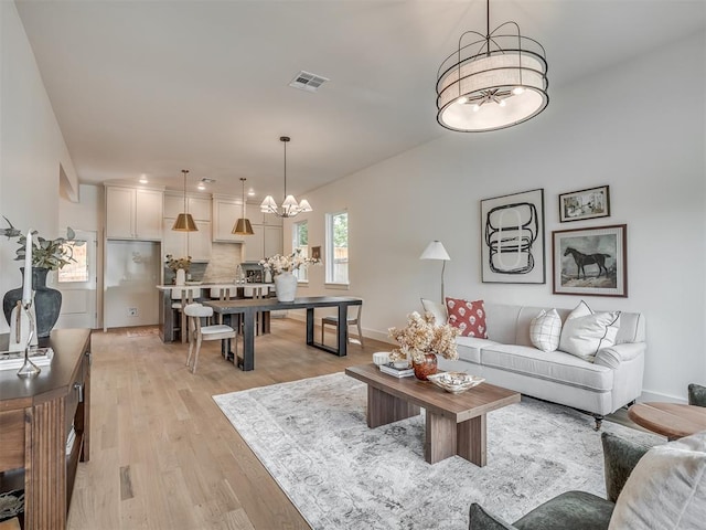 living room with an inviting chandelier, light wood-type flooring, visible vents, and baseboards