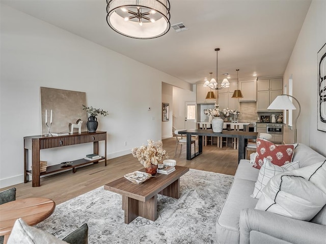 living room featuring light wood-type flooring, visible vents, baseboards, and a notable chandelier