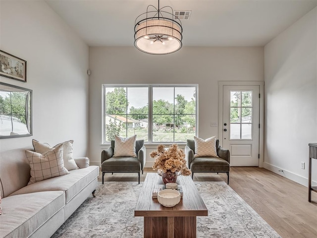 living room featuring an inviting chandelier, a wealth of natural light, visible vents, and light wood-style floors