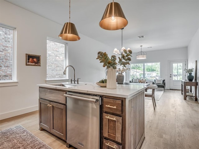 kitchen featuring decorative light fixtures, dishwasher, light wood finished floors, a sink, and a kitchen island with sink