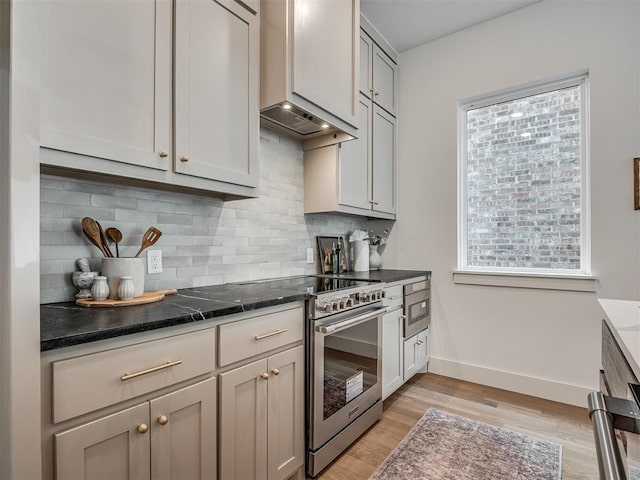 kitchen featuring dark stone countertops, light wood-type flooring, baseboards, high end range, and decorative backsplash