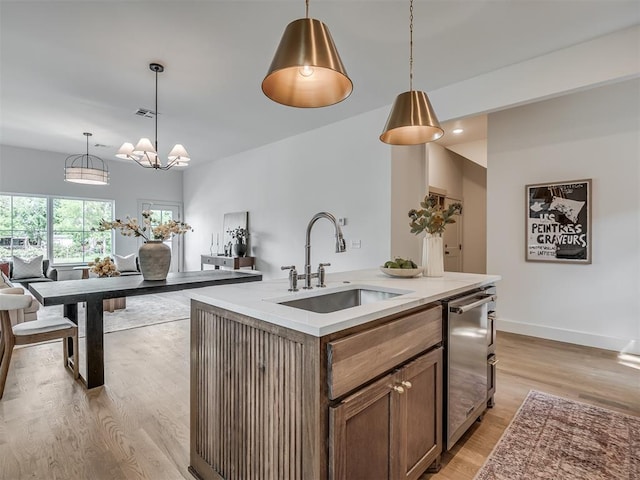 kitchen featuring a sink, dishwasher, light wood-style flooring, light countertops, and hanging light fixtures