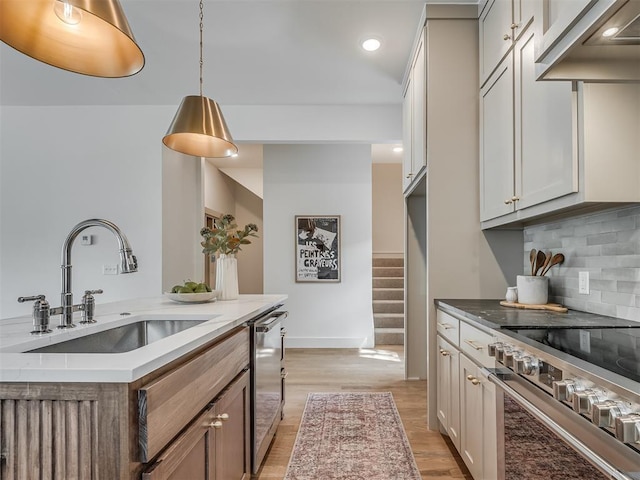 kitchen featuring baseboards, a sink, backsplash, light wood-style floors, and appliances with stainless steel finishes