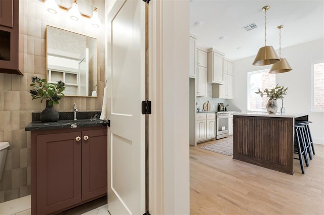kitchen featuring decorative light fixtures, a breakfast bar area, visible vents, light wood finished floors, and high end stainless steel range oven