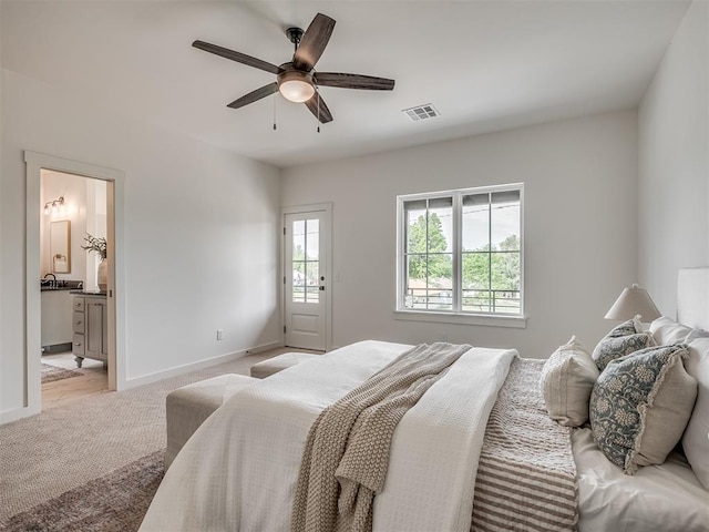 bedroom featuring a ceiling fan, visible vents, baseboards, light colored carpet, and ensuite bath
