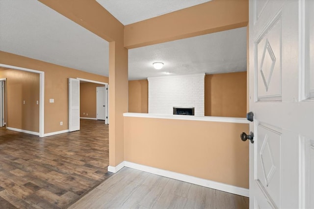 interior space with baseboards, wood finished floors, a brick fireplace, and a textured ceiling