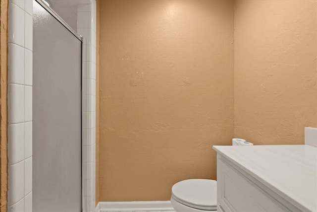 full bath with a shower with shower door, toilet, a textured wall, and baseboards