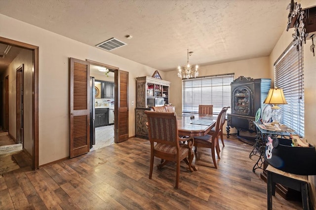 dining room featuring hardwood / wood-style floors, an inviting chandelier, visible vents, and a textured ceiling