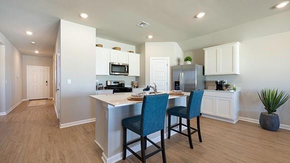 kitchen with a kitchen bar, light wood finished floors, an island with sink, stainless steel appliances, and light countertops