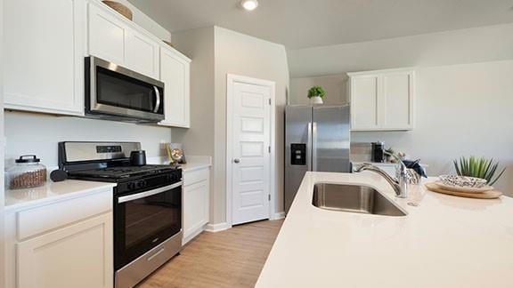 kitchen featuring a sink, stainless steel appliances, light countertops, white cabinets, and light wood-type flooring
