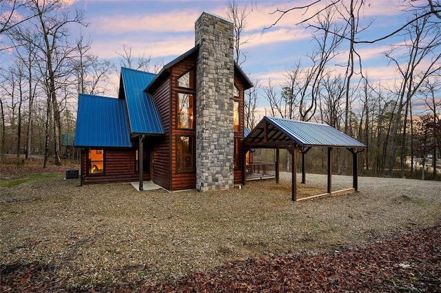 view of side of home with faux log siding, a gazebo, metal roof, a chimney, and a carport