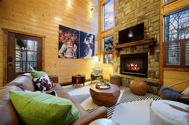 living room with wood walls, a stone fireplace, and a high ceiling
