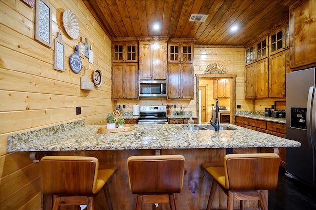kitchen featuring appliances with stainless steel finishes, a sink, wood ceiling, wooden walls, and light stone countertops