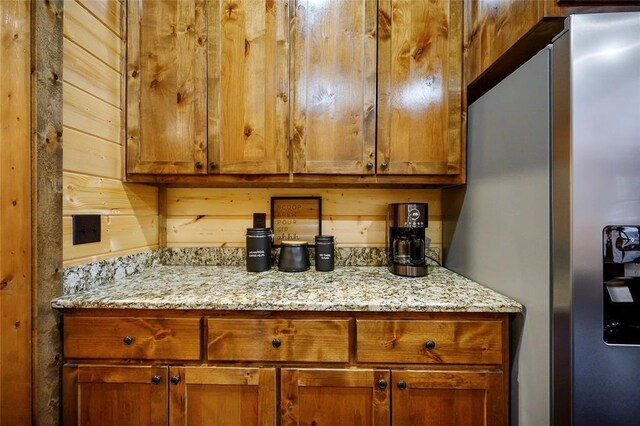 kitchen with stainless steel fridge, light stone countertops, and brown cabinets
