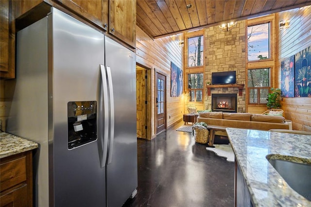 kitchen featuring stainless steel fridge, wooden walls, wood ceiling, light stone counters, and a fireplace